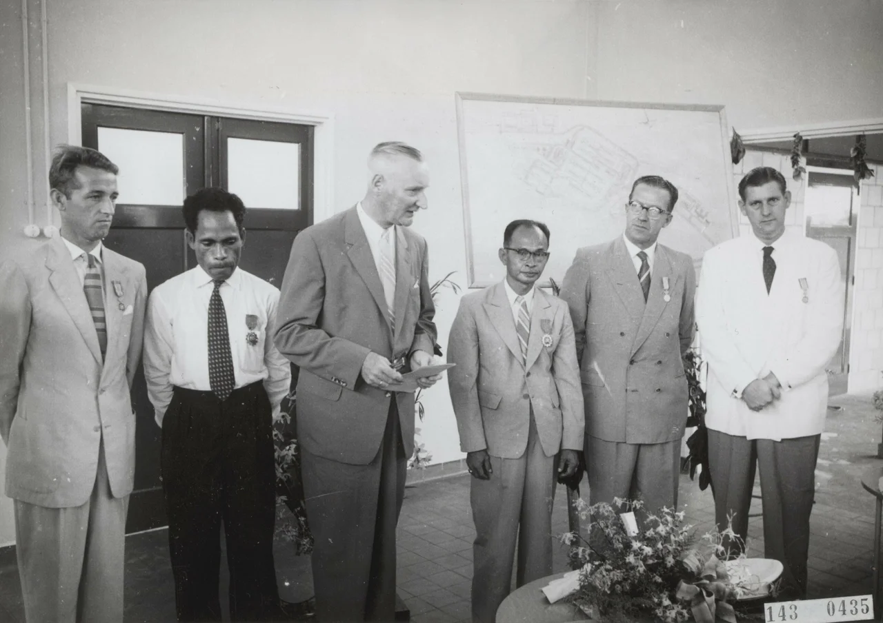 Opening Centraal Ziekenhuis te Hollandia - Nederlands Nieuw Guinea: Uitreiking decoraties. Van links naar rechts: 1. men. Petersen, Opzichter bouw Ziekenhuis (in dienst van het Gouvernement): Koninklijke Onderscheiding, 2. men. Rumainum: Onderscheiding van het Gouvernement, 3. men. Zuiderhoek: Hoofd Dienst van Volksgezondheid houdt toespraak, 4. men. Mandosir: Onderscheiding van het Gouvernement, 5. men. ? : Uitvoerder (in dienst van samenwerkende bouwonderneming): Koninklijke Onderscheiding, 6. men. Gerrit Palsgraaf: Hoofduitvoerder Bouwmij Hollandia BMH: Koninklijke Onderscheiding.