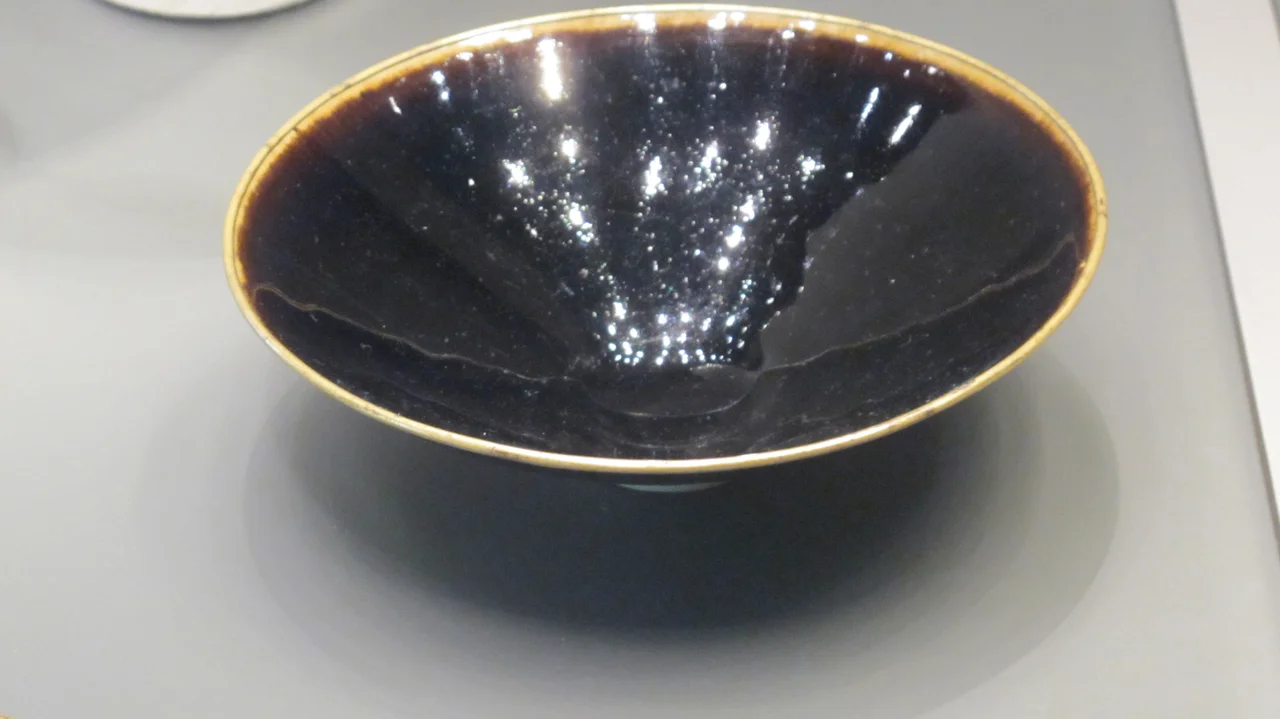 Black glazed tea-bowl. AD 1000-1127. Northern Song dynasty. Quyang, Ding prefecture, Hebei province. Sir Percival David Collection, British Museum. Quotation of the museum : Ding potters manufactured vessels of exquisite quality with pure white bodies, but also added coloured glazes. This example is coated in a solution rich in iron-oxide which, when fired, gives it a glossy ink-black color. Song dynasty writers celebrated black and brown wares, associating them with luxurious lacquer wares. It has a copper rim which enhances its status.
